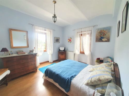 Spacious bedroom in French gîte cottage with blue bedding, wooden furniture, mountain views, and hardwood floors near