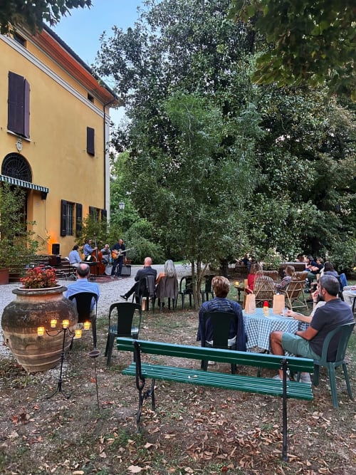 Cortile all'aperto di Palazzo Bonfiglioli con ospiti che cenano, musica dal vivo, riscaldatore illuminato e lussureggiante vegetazione a San