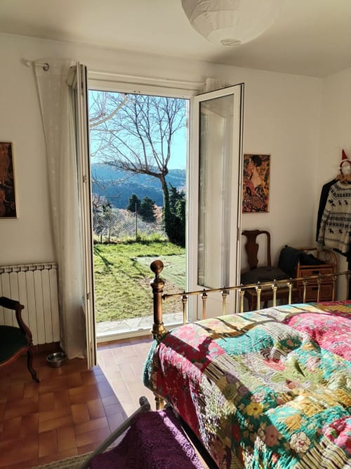 Bedroom with mountain views through French doors opening to garden, brass bed, colorful patchwork quilt, white radiator,