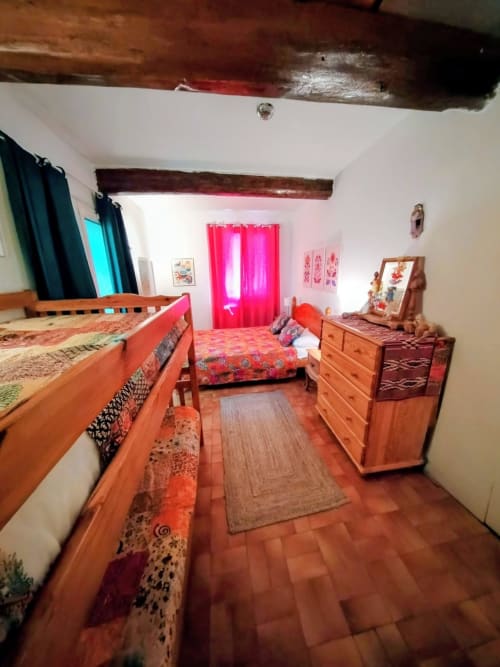 Spacious bedroom in French villa with wooden beds, orange tiled floor, pink curtains, and rustic wooden beam ceiling