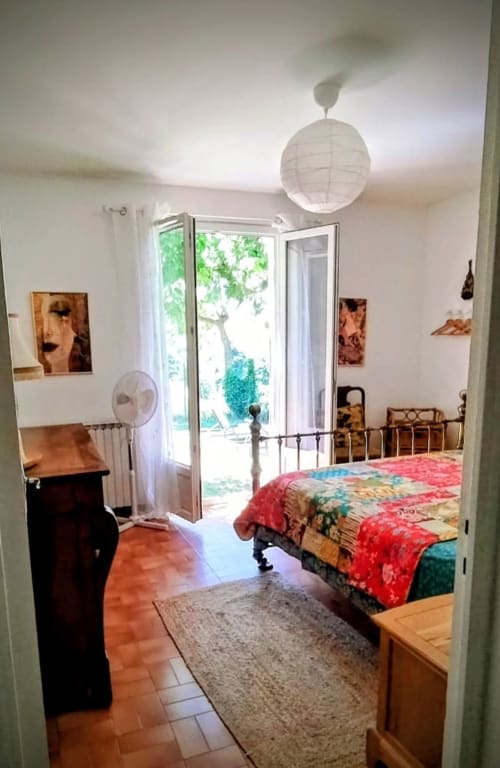 Bright bedroom in French villa with colorful patchwork bed, French doors opening to garden, mountain views, and white paper