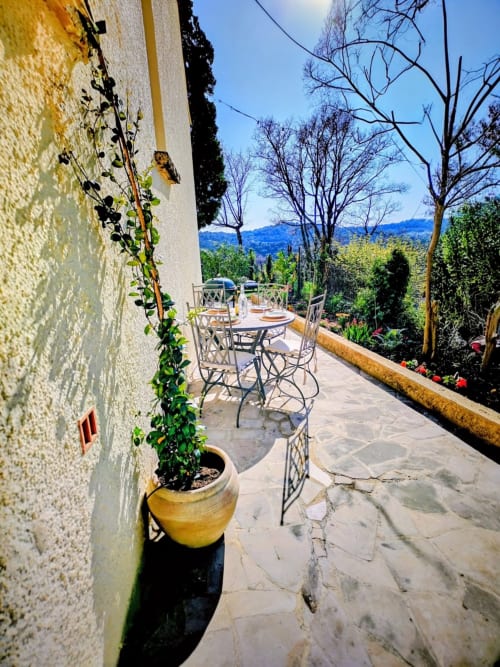 Sunny terrace with dining area, ivy-covered stone wall, and mountain views at French villa near Nyons