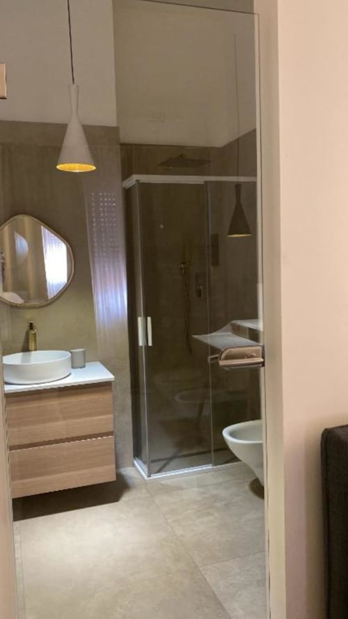 Bagno moderno presso B&B Il Giardino di Ulisse a Reggio Calabria con lavabo a bacinella, doccia con box in vetro e lampada a sospensione