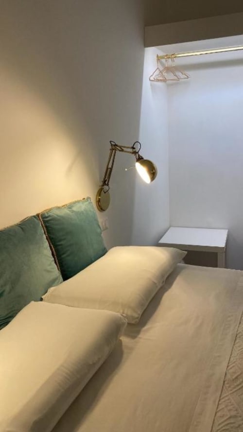 Camera moderna al B&B Il Giardino di Ulisse a Reggio Calabria con biancheria color crema, cuscino verde, lampada in ottone e stile minimalista