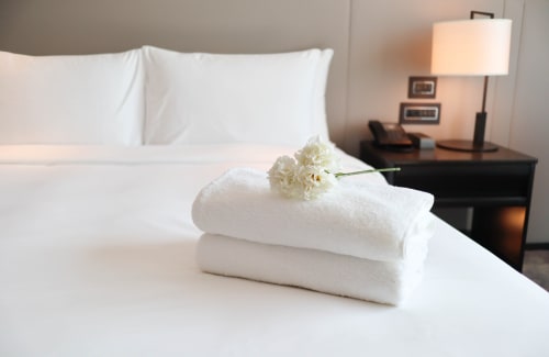 Camera da letto di lusso al Palazzo di Donna con asciugamani bianchi arrotolati e fiore bianco sul letto, lampada sul comodino