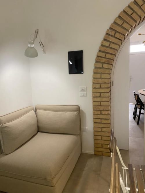Camera accogliente del B&B Il Giardino di Ulisse con divano beige, arco in mattoni, lampada a sospensione e TV a Reggio Calabria