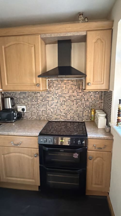 Modern kitchen with wooden cabinets, black cooker, mosaic backsplash, and range hood at England Furnished Homes in High