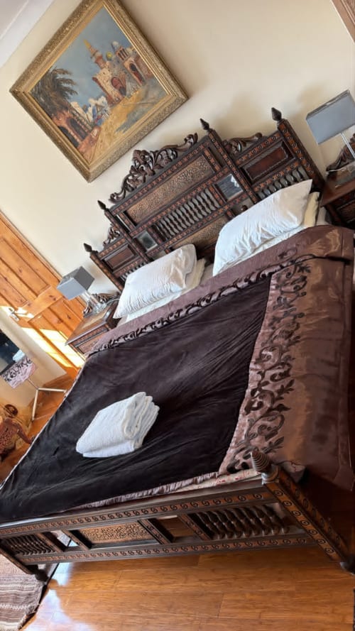 Ornate wooden bed with decorative carved headboard, white pillows, dark bedding in High Wycombe furnished property