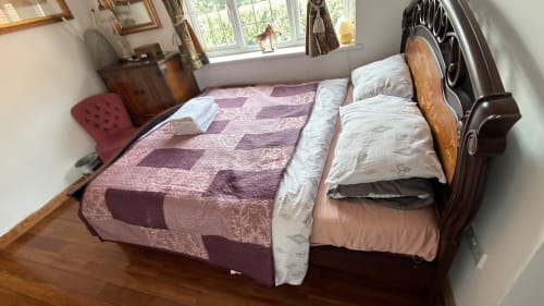 Comfortable bedroom with wooden bed, purple bedding, white pillows, wooden dresser, and garden view windows at England