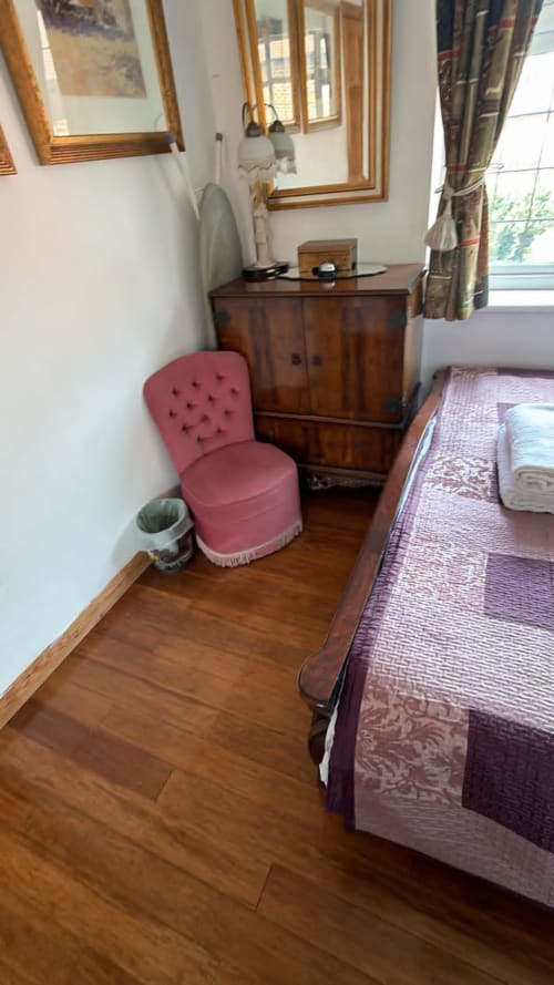 Cozy bedroom in High Wycombe furnished home with pink chair, wooden dresser, bed, and garden view window