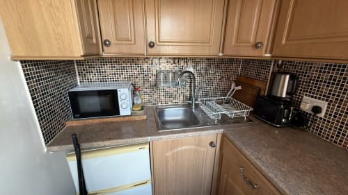 Compact kitchen with wooden cabinets, black tile backsplash, microwave, sink, and countertop appliances in High Wycombe