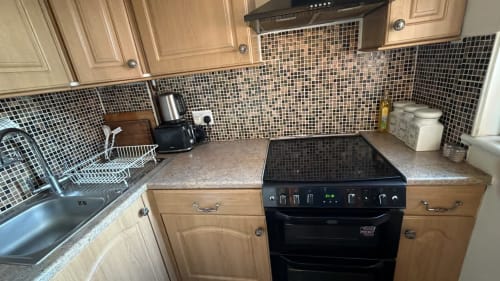 Modern kitchen with black mosaic backsplash, electric range, light wood cabinets, and gray countertops in furnished High