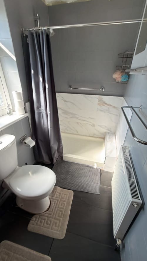 Modern bathroom with walk-in shower, toilet, radiator, and dark tile flooring at England Furnished Homes in High Wycombe