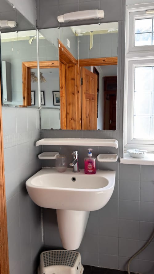 Modern bathroom with pedestal sink, large mirror, and gray tile walls at England Furnished Homes in High Wycombe
