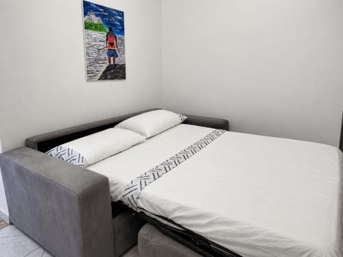 Camera moderna dell'Hotel Palazzo di Donna con divano letto grigio, biancheria bianca e opere d'arte costiera