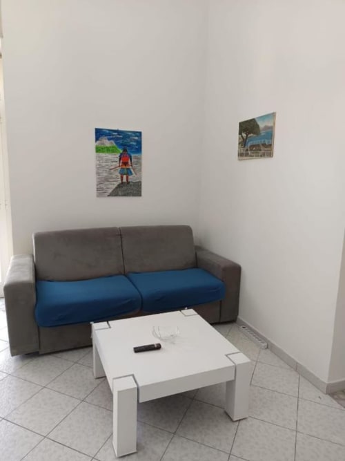 Soggiorno moderno a Palazzo di Donna con divano grigio, cuscini blu, tavolino bianco e opere d'arte costiera su pareti bianche
