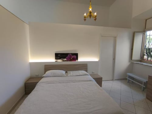 Modern bedroom at Palazzo di Donna hotel with wooden bed, white linens, illuminated headboard shelf, and elegant gold