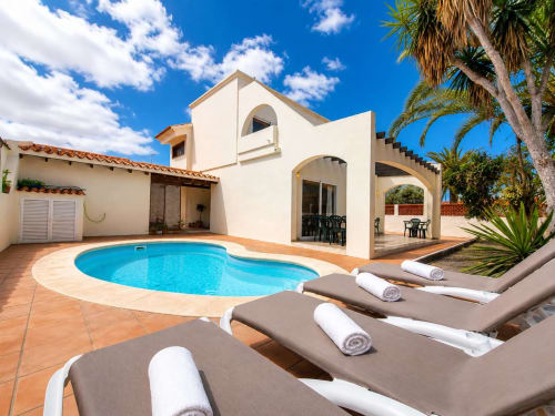 Villa de lujo con piscina azul, tumbonas, terraza y palmeras en Corralejo, Fuerteventura