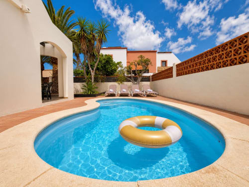 Piscina circular con flotador dorado en Villa Paloma en Corralejo, Fuerteventura, rodeada de tumbonas y palmeras