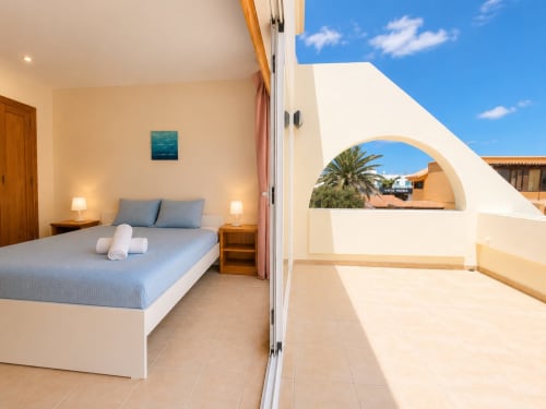 Dormitorio luminoso en Villa Paloma de Sara & Gino, Corralejo Fuerteventura, con vistas a la terraza y palmeras