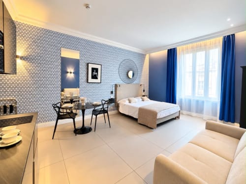 Modernes Zimmer im SEVEN SUITES SANREMO mit blauen gemusterten Wänden, Bett, Schreibtisch und Stadtblick aus den Fenstern in Sanremo, Italien