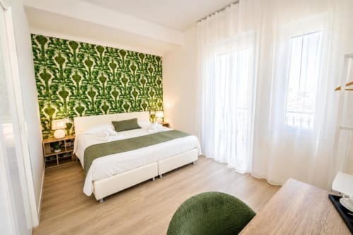 Camera doppia deluxe Le Rooms in Italia con testata damascata verde, biancheria bianca, porte-finestre e pavimento in legno