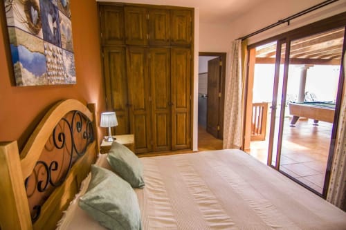 Hauptschlafzimmer der Villa Rodrigo im Sara & Gino Fuerteventura, Corralejo, mit Holzbett, Zugang zur Terrasse und Poolblick