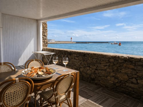 Terrasse d'appartement en bord de mer à Guilvinec avec plateau de fruits de mer, verres de vin et vue sur le port et le phare