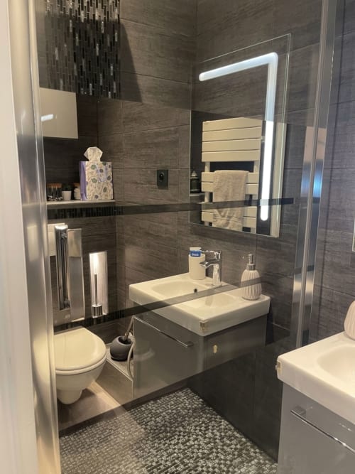 Salle de bain moderne avec lavabos doubles, miroir lumineux, carrelage sombre et toilettes au Paradis Des Logis