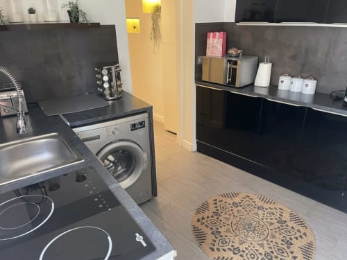 Cuisine moderne avec lave-linge, plaque de cuisson électrique, armoires noires et tapis décoratif de l'appartement Le Saint Brice