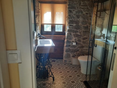 Baño moderno en apartamento Bikarte Alojamientos con paredes de piedra, ducha independiente, inodoro y piso con patrón