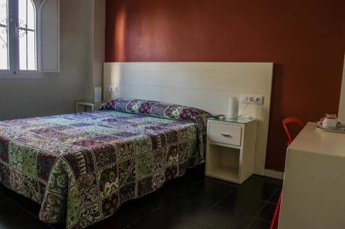 Habitación con cama Queen en Hostal San Vicente II, Sevilla, con ropa de cama estampada, cabecero crema y paredes burdeos