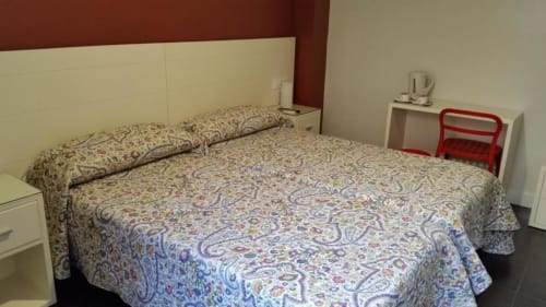Habitación con cama queen del Hostal San Vicente II en Sevilla con ropa de cama estampada y cabecero color crema