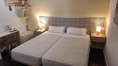 Cama doble en habitación económica del Hostal San Vicente II, Sevilla con cabecera estampada y lámparas de noche