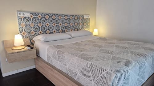 Dormitorio moderno en Hostal San Vicente II de Sevilla con cabecero estampado, ropa de cama blanca y mesillas de noche con lámparas