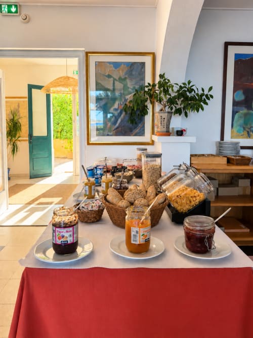 Buffet petit-déjeuner de l'Hôtel Thalassa à Cargèse avec viennoiseries, confitures et pains sur table aux nappes rouges
