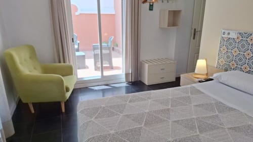 Habitación moderna del Hostal San Vicente II en Sevilla con sillón amarillo, vista a la terraza y ropa de cama estampada