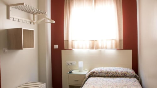 Habitación individual en Hostal San Vicente II de Sevilla con cama sencilla, ventana, paredes con toques rojos y mobiliario básico.
