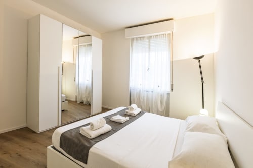 Camera moderna nell'appartamento Solumnia Milano con armadio bianco, letto matrimoniale e finestre con vista città