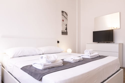 Camera moderna in Solumnia Urban Nest 2, Milano con letto bianco, asciugamani, TV e arredamento minimalista