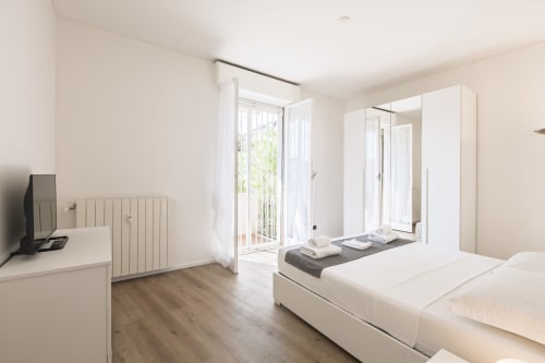 Camera moderna a Solumnia Urban Nest 2 a Milano con letti matrimoniali, armadio bianco, pavimenti in legno e vista balcone sulla città