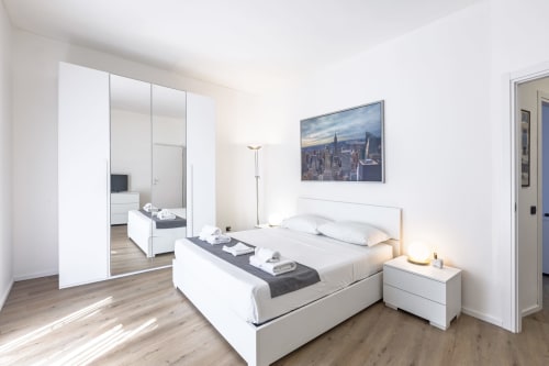 Camera moderna presso Solumnia Urban Nest 2 a Milano con armadio a specchio, letto bianco e quadri dello skyline cittadino