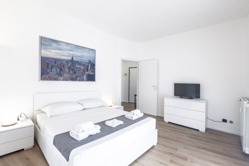 Camera moderna nell'appartamento Solumnia Urban Nest a Milano, con letto bianco, opera skyline, TV e pavimenti in legno