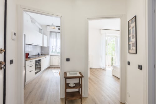 Luminoso ingresso di un appartamento milanese con cucina, tavolino in legno e corridoio che conduce alla zona living con accesso al balcone