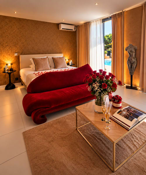 Suite luxueuse à La Villa Monarque avec canapé en velours rouge, vue sur la piscine et ambiance dorée à Cap d'Agde