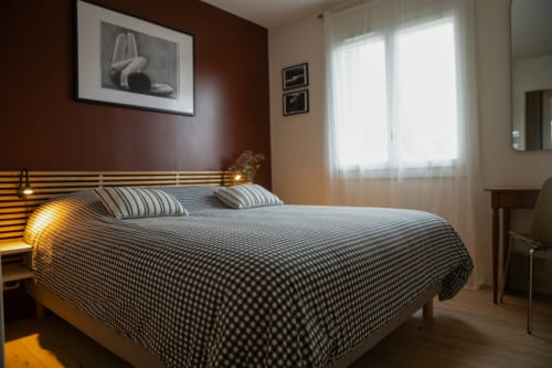 Chambre moderne du gîte Recevoir par Charline à Biganos, avec lit à rayures, éclairage chaleureux et vue sur le jardin