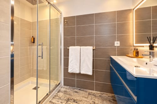 Salle de bain moderne à l'hôtel La Villa Monarque avec douche spacieuse, meuble vasque bleu et sèche-serviettes chauffant à Cap d'Agde