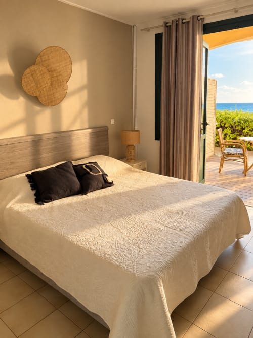 Chambre lumineuse en bord de mer à l'Hôtel Thalassa Cargèse avec vue sur la mer, literie crème et décoration murale tissée