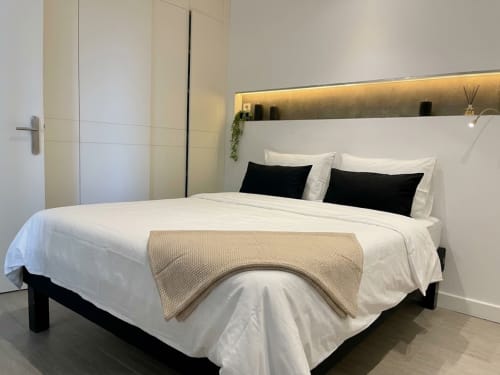 Chambre moderne au Paradis Des Logis avec literie blanche, oreillers noirs et éclairage ambiant chaleureux à Saint-Brice-sous-Forêt