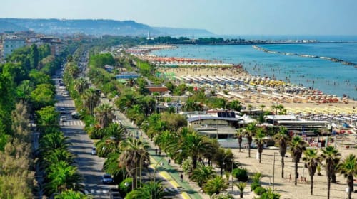 Le Rooms B&B affaccia su una spiaggia italiana vibrante con palme, costa sabbiosa e acque del Mediterraneo sotto un cielo sereno